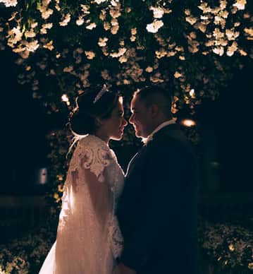 Casal se abraça sob flores brancas; comemoração romântica à noite. Bride's Dream