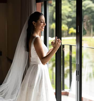 Noiva sorridente de véu branco e vestido, contemplando o cenário do evento Bride's Dream