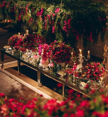 Mesa de espelho com flores e velas vermelhas, compondo a decoração da cerimônia.