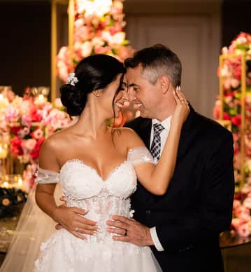 Casal sorridente comemorando o casamento, ao lado de bolo floral, Bride's Dream.